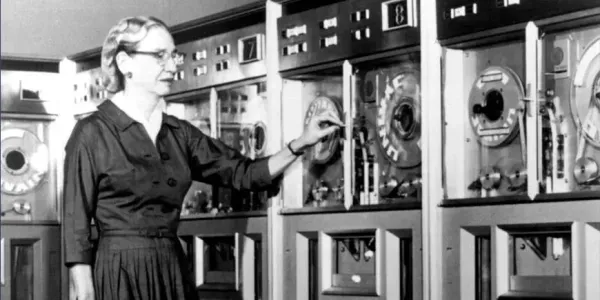 Grace Hopper, who originated the convention of calling errors in code "bugs", looks at some old-fashioned tape machines.